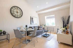 A modern living room with a dining area, a large wall clock, and a window with natural light. - Newly Renovated 1BDR in Knightsbridge with WiFi (London)
