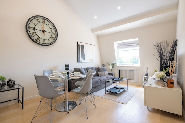 Una sala moderna con comedor, un reloj de pared grande y una ventana con luz natural.