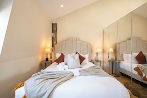 Una habitación de hotel con una cama grande, mesitas de noche con lámparas, un espejo y una estantería en la pared con libros.