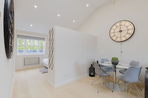 A modern dining area with a round table, chairs, and a wall clock.