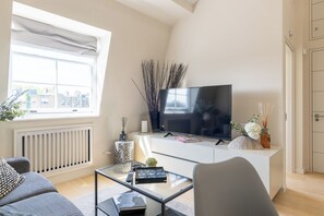 A modern living room with a large flat-screen TV, a sofa, a coffee table, and a radiator. - Newly Renovated 1BDR in Knightsbridge with WiFi (London)