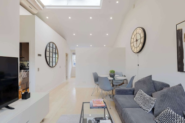 Un salon moderne doté d’un téléviseur à écran plat, d’un canapé, d’une table basse et d’un coin repas avec des chaises et une table.