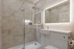A modern bathroom with a glass-enclosed shower, a large mirror, and a vanity with a sink and cabinet. - Newly Renovated 1BDR in Knightsbridge with WiFi (London)