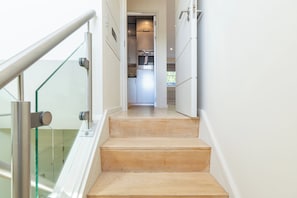 Una escalera conduce a una zona de cocina con electrodomésticos modernos y una barandilla de cristal.