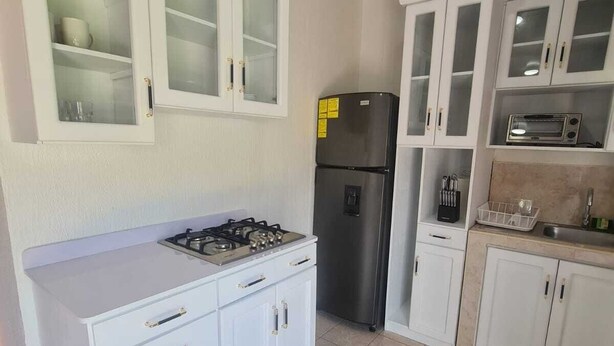A kitchen with white cabinets, a gas stove, a black refrigerator, and a microwave. - Silvia House II Acropoli Sonsonate. (Sonsonate)