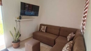 A living room with a brown sectional sofa, a small potted plant, and a flat-screen TV mounted on the wall. - Silvia House II Acropoli Sonsonate. (Sonsonate)
