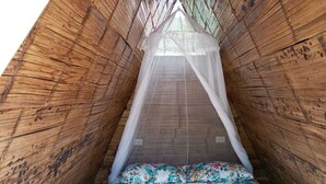 Une pièce triangulaire en bois, avec un lit et une moustiquaire.