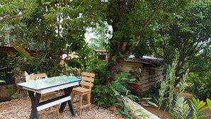 Un espace extérieur aménagé avec une table et des chaises, entouré d’une végétation luxuriante et d’une petite structure en bois.
