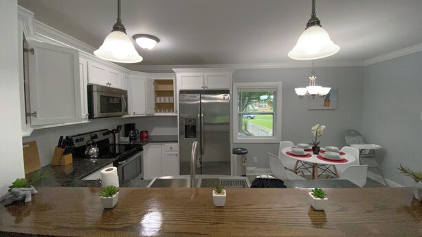 Een moderne keuken met witte kastjes, roestvrijstalen apparatuur, een houten aanrechtblad en hanglampen.