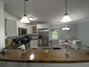A modern kitchen with white cabinets, stainless steel appliances, a wooden countertop, and pendant lighting.