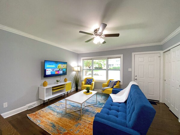 A living room with a blue sofa, yellow chairs, a white coffee table, and a ceiling fan.