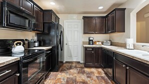 A kitchen with dark wood cabinets, a black refrigerator, a microwave, a stove, and a coffee maker. - Sleeps 9, Pet Friendly, Workspace, Easy Access to Dining and Shops (Meridian)