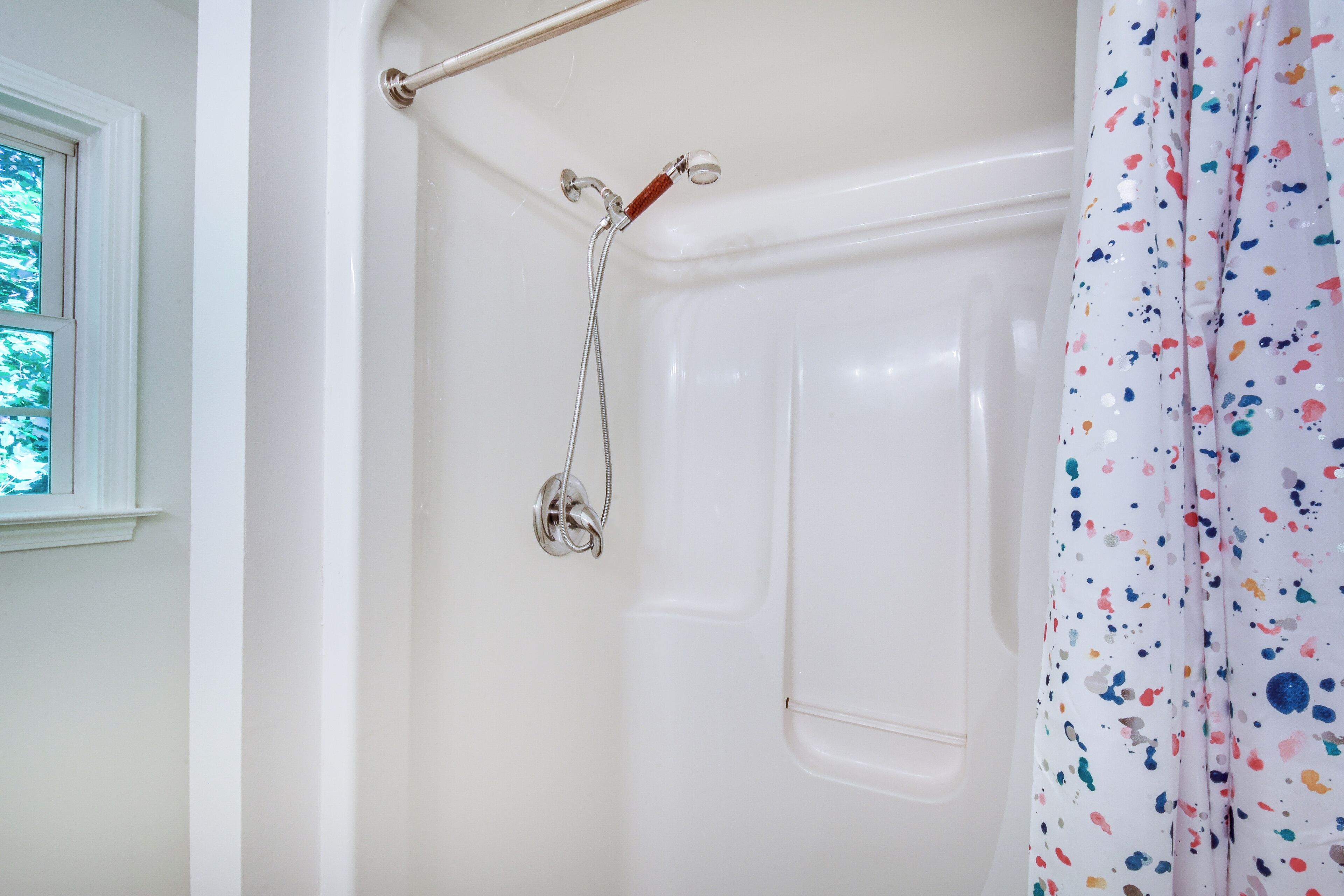 A bathroom with a shower, a window, and a curtain.