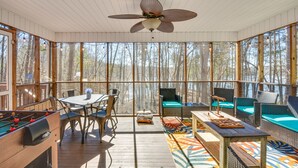 Ein sonnendurchflutetes Zimmer mit Tischfußballtisch, Sitzgelegenheit und großen Fenstern mit Blick auf einen Wald.