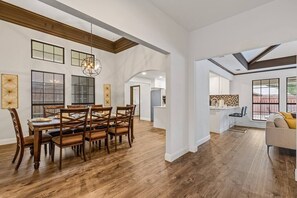 A spacious dining area with a wooden table and chairs, a chandelier, and large windows.