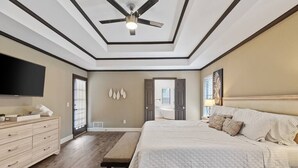 Une chambre avec un grand lit, un ventilateur de plafond, une télévision et un banc.