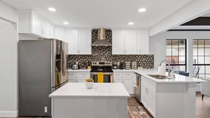 Une cuisine moderne avec des meubles blancs, un réfrigérateur en acier inoxydable, un îlot central et un pare-feu décoratif.