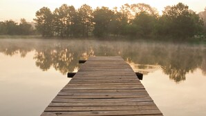 A wooden pier extending into calm water with trees in the background. - Log cabin overlooking a private lake on a working farm (Daingerfield)