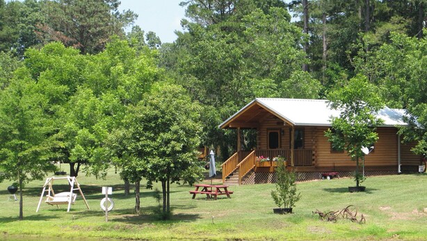 A cabin with a porch, picnic table, and swing set by a lake. - Log cabin overlooking a private lake on a working farm (Daingerfield)