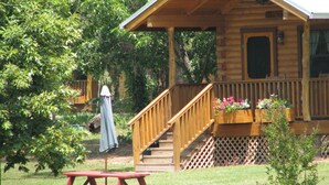 A wooden cabin with a porch, a picnic table, and a covered umbrella. - Log cabin overlooking a private lake on a working farm (Daingerfield)