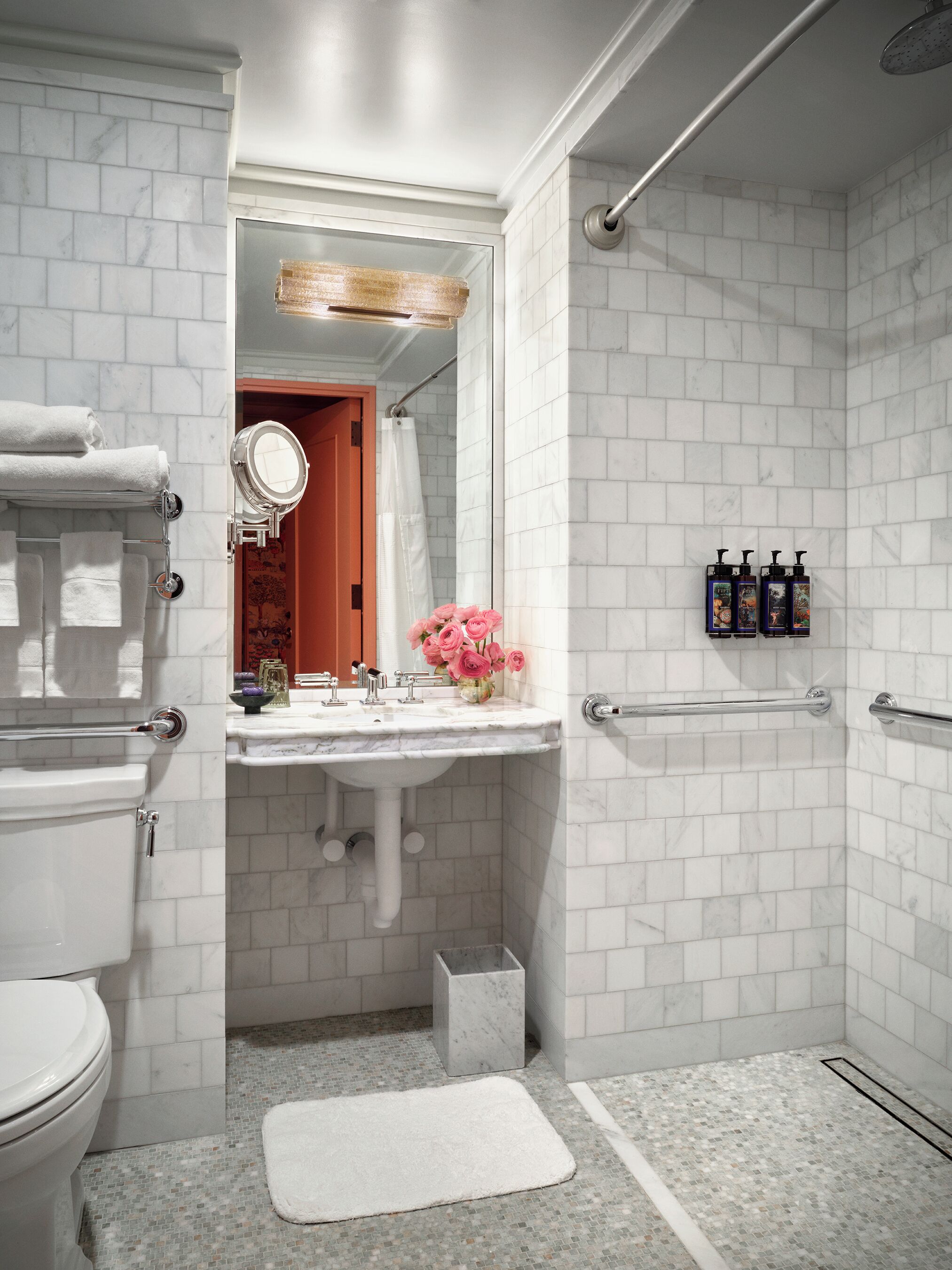 A bathroom with a white tiled shower, a sink with a mirror, and a toilet.