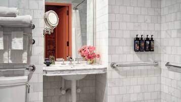 A bathroom with a white tiled shower, a sink with a mirror, and a toilet.