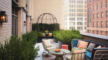 A rooftop terrace with outdoor seating, a decorative metal sphere, and a view of surrounding buildings.