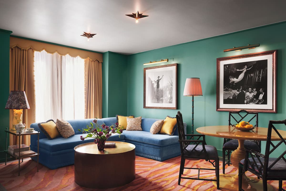 A living room with a blue sofa, a round coffee table, a dining table with chairs, and two framed pictures on the wall.