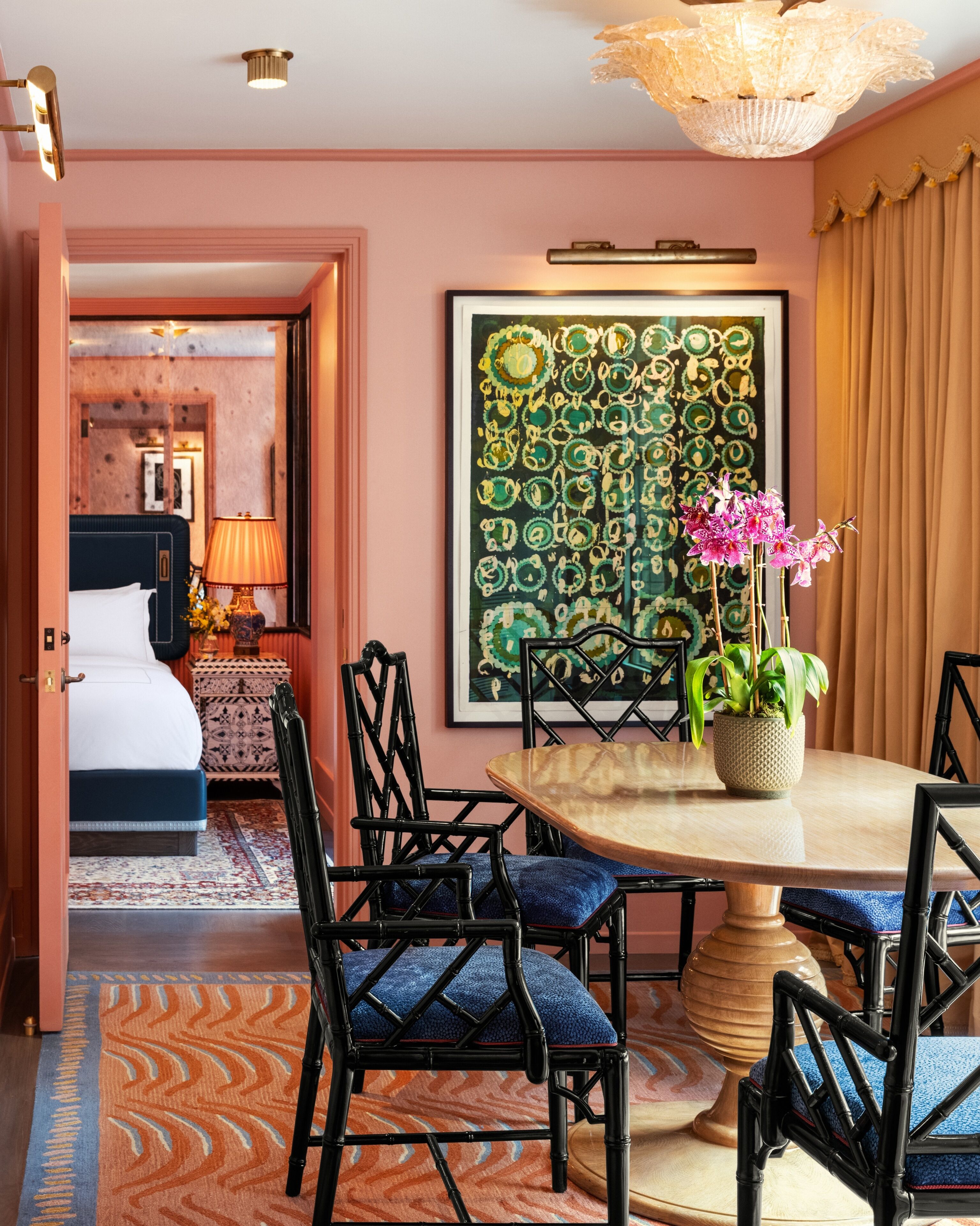 Habitación de hotel con zona de comedor, cama, un cuadro abstracto grande y una planta en maceta.