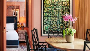 Habitación de hotel con zona de comedor, cama, un cuadro abstracto grande y una planta en maceta.