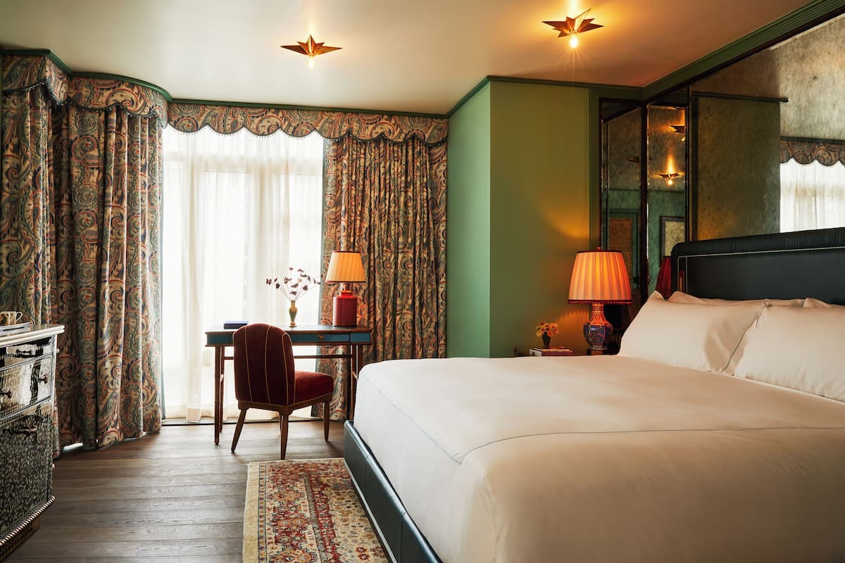 A hotel room with a large bed, a desk with a chair, a lamp, and curtains.
