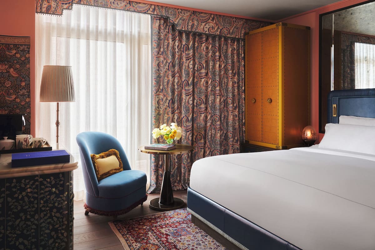 A hotel room with a bed, a chair, a small table with a lamp, and a decorative vase.