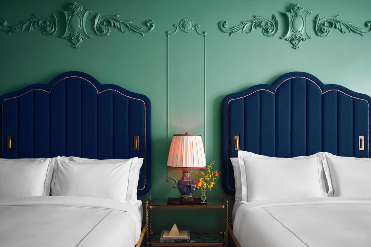 A room with two beds, a nightstand with a lamp, and decorative wall moldings.