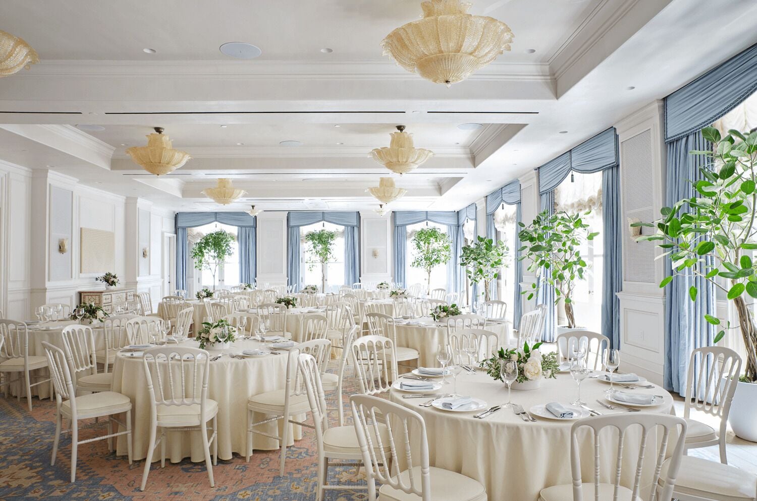 Un salón de banquetes con mesas redondas, sillas blancas y candelabros.