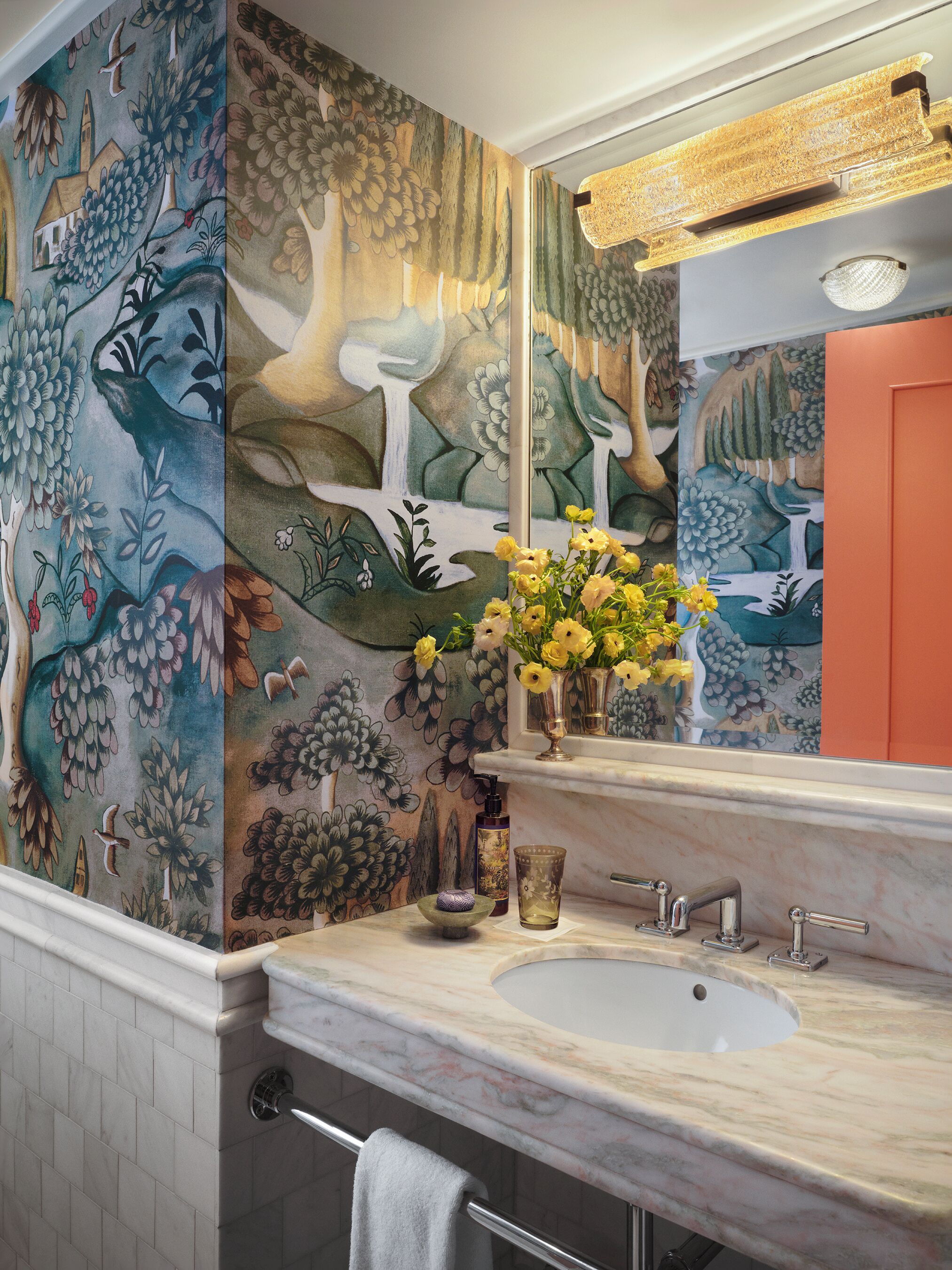 A bathroom with a marble sink, a mirror, a vase with yellow flowers, and a wall mural.