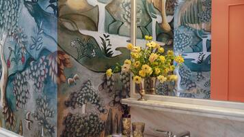 A bathroom with a marble sink, a mirror, a vase with yellow flowers, and a wall mural.