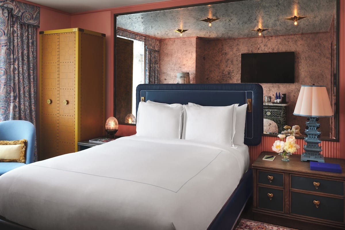 A hotel room with a large bed, a nightstand, a lamp, a dresser, and a mirror.