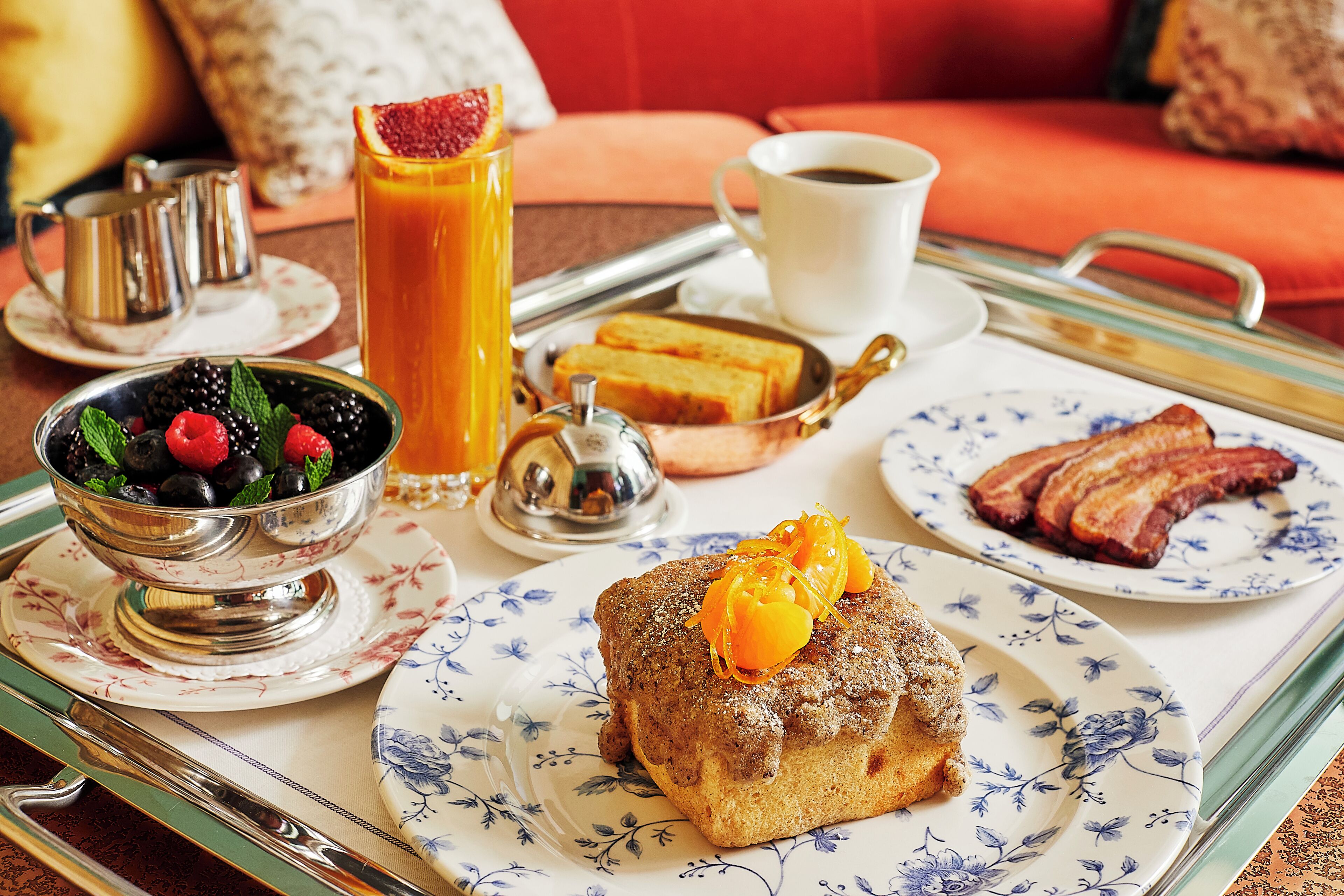 Un plateau de petit-déjeuner avec des toasts, du bacon, un muffin, un assortiment de fruits et une tasse de café.