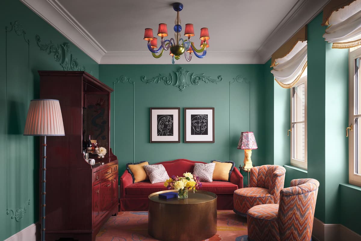 A room with a red sofa, a patterned armchair, a round coffee table, a floor lamp, and a chandelier.