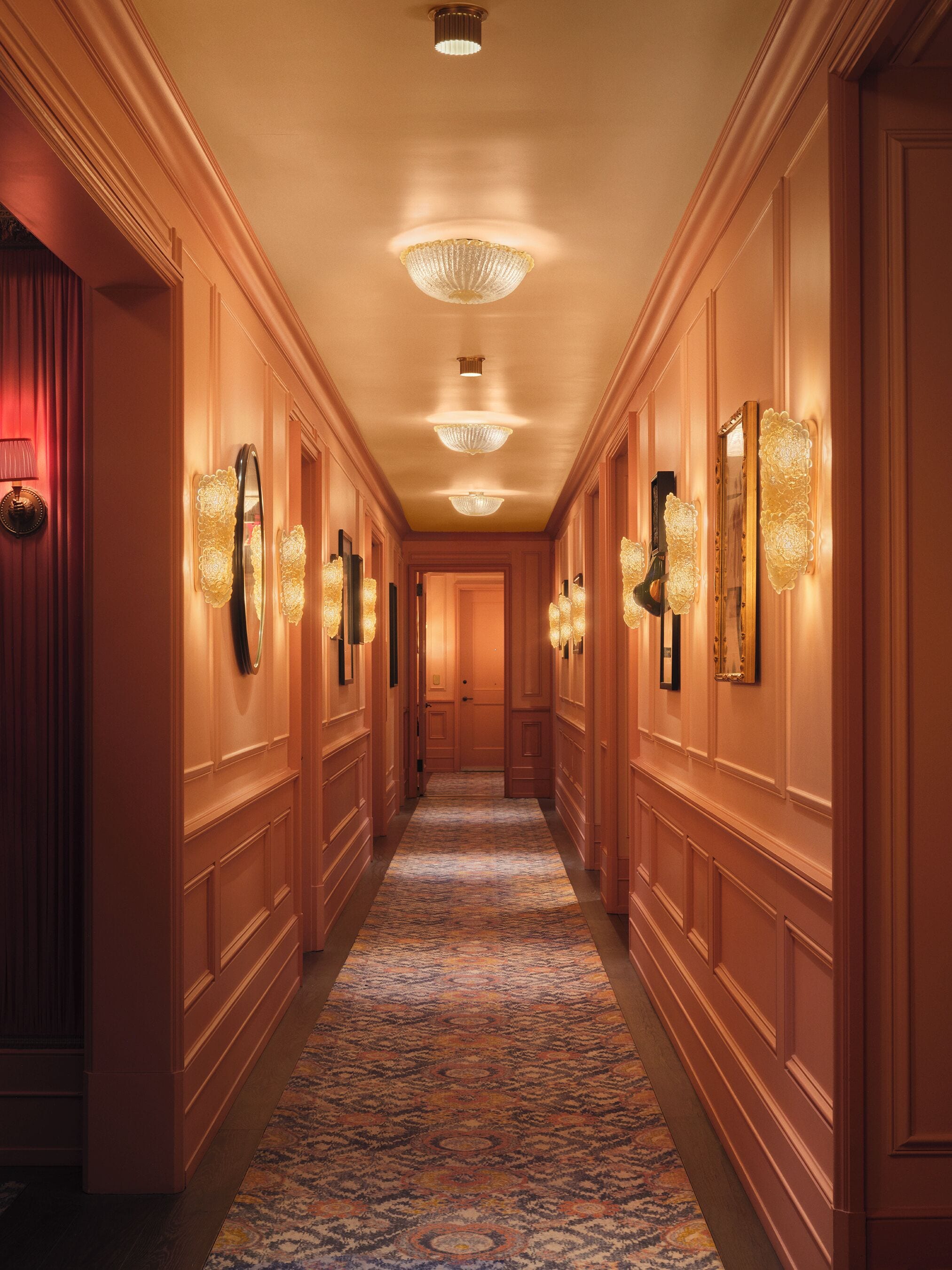 A hotel hallway with ornate wall sconces, a patterned carpet, and a polished wooden floor.