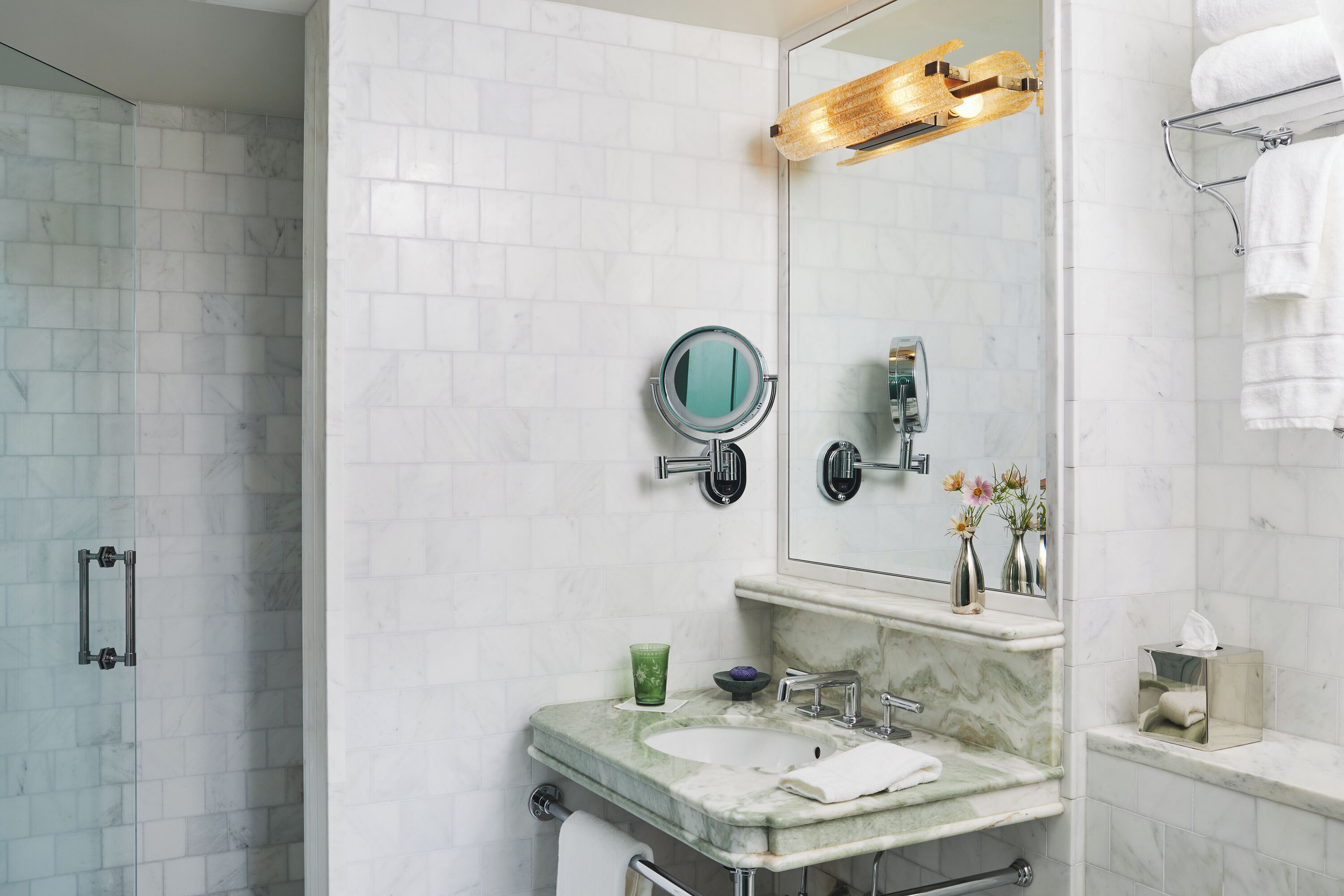 A bathroom with a glass shower enclosure, a marble sink, a mirror, and a towel rack.