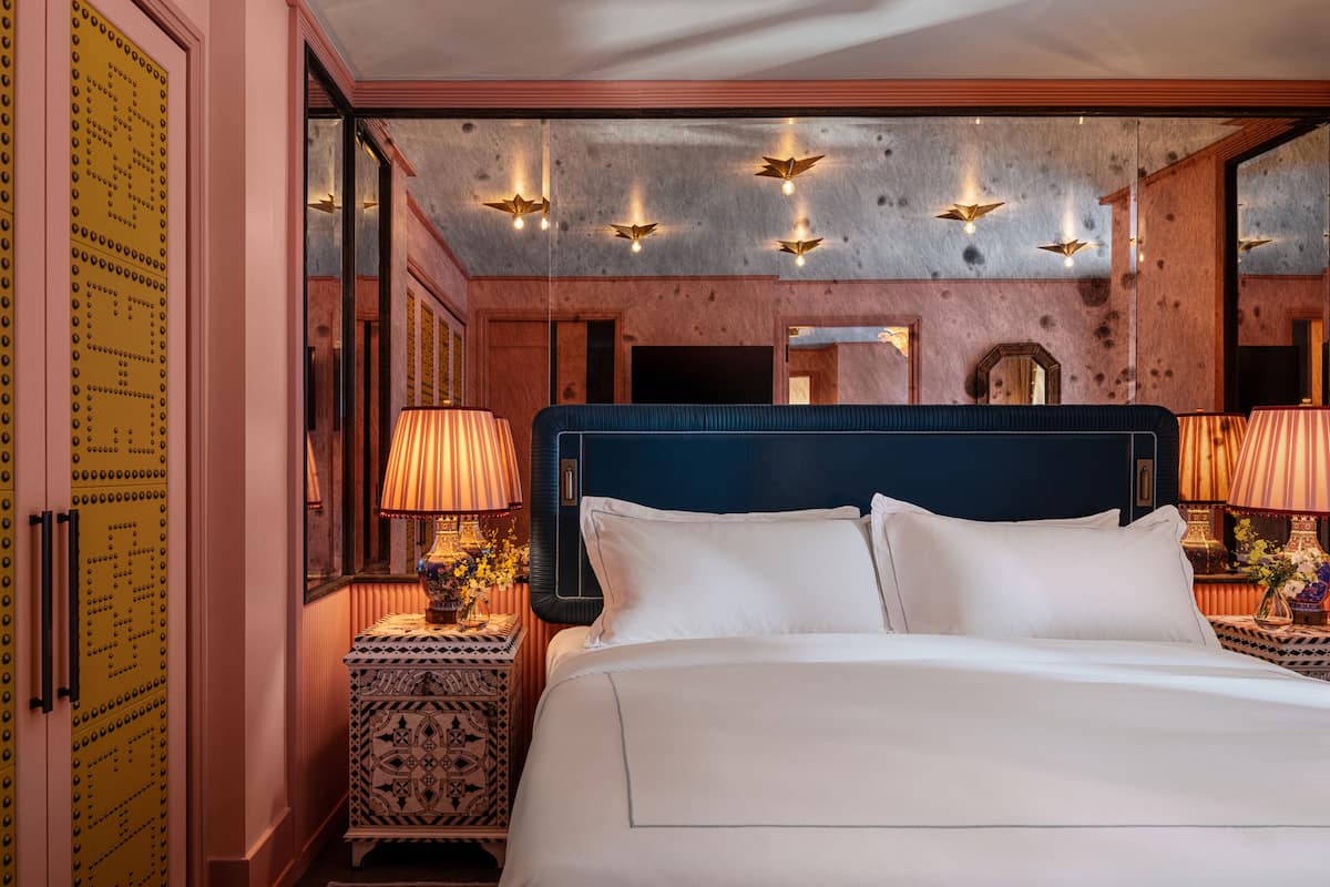 A hotel room with a large bed, two bedside lamps, a patterned nightstand, a mirror, and a decorative wall.