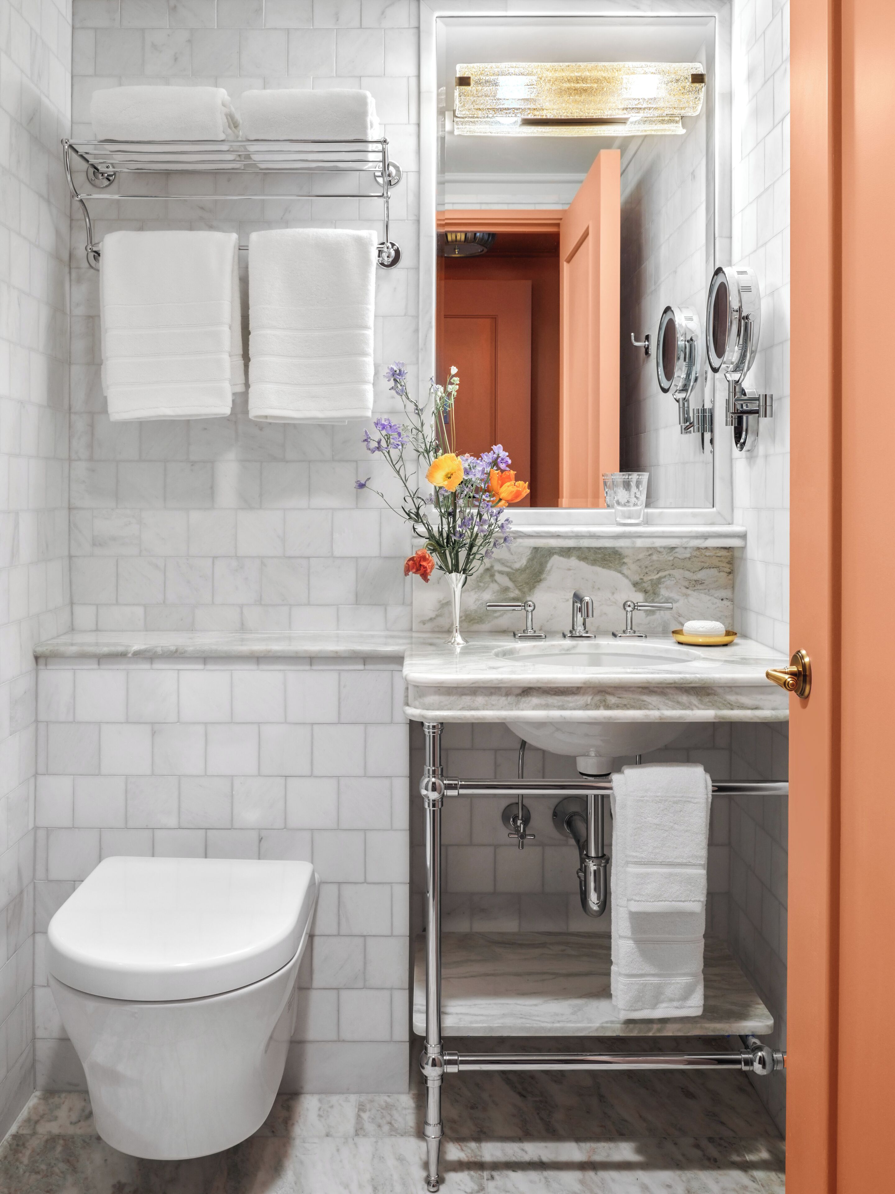 A bathroom with a white toilet, a marble sink, a mirror, and a towel rack with towels.