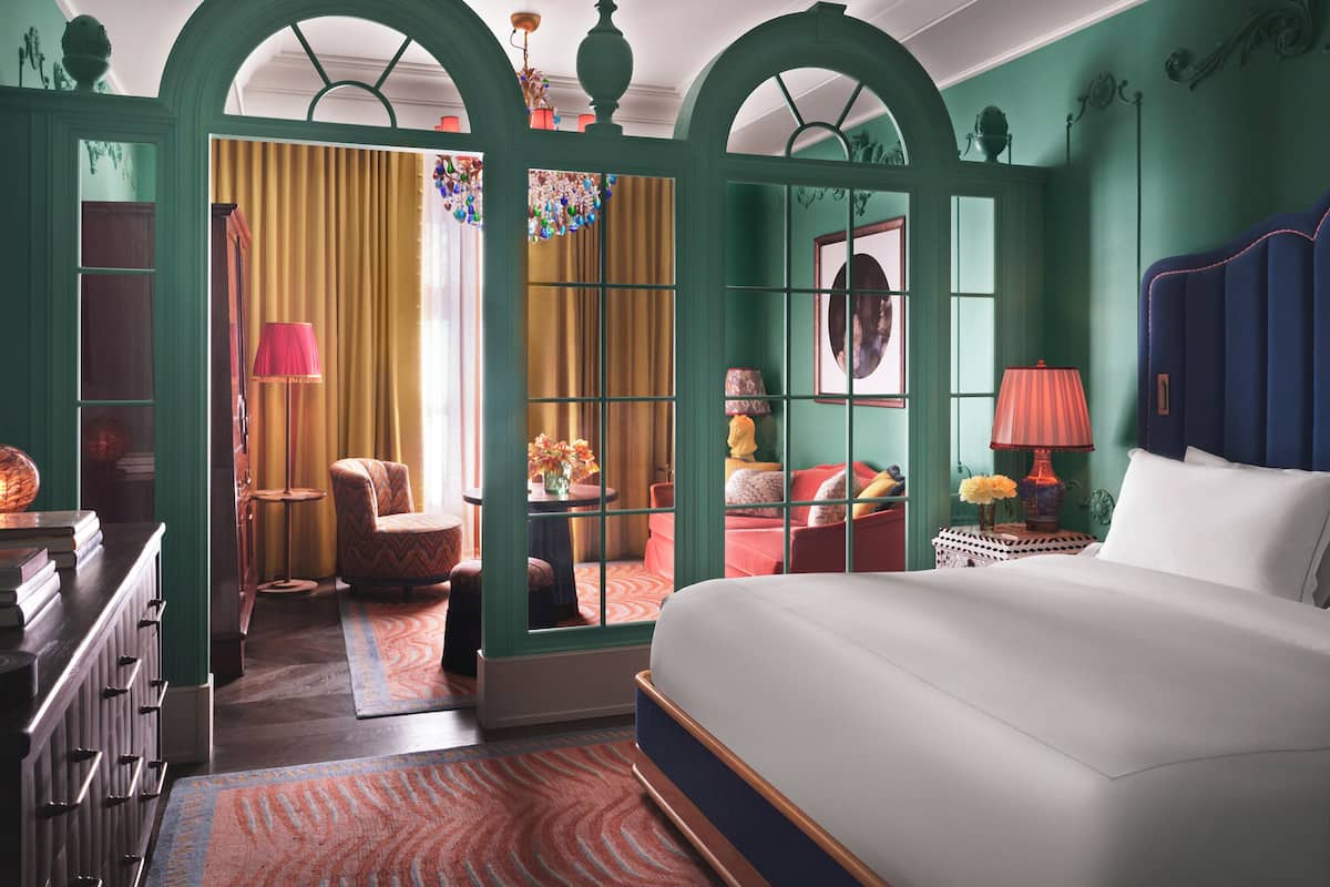 A bedroom with a large bed, a chair, a table, and a mirror.