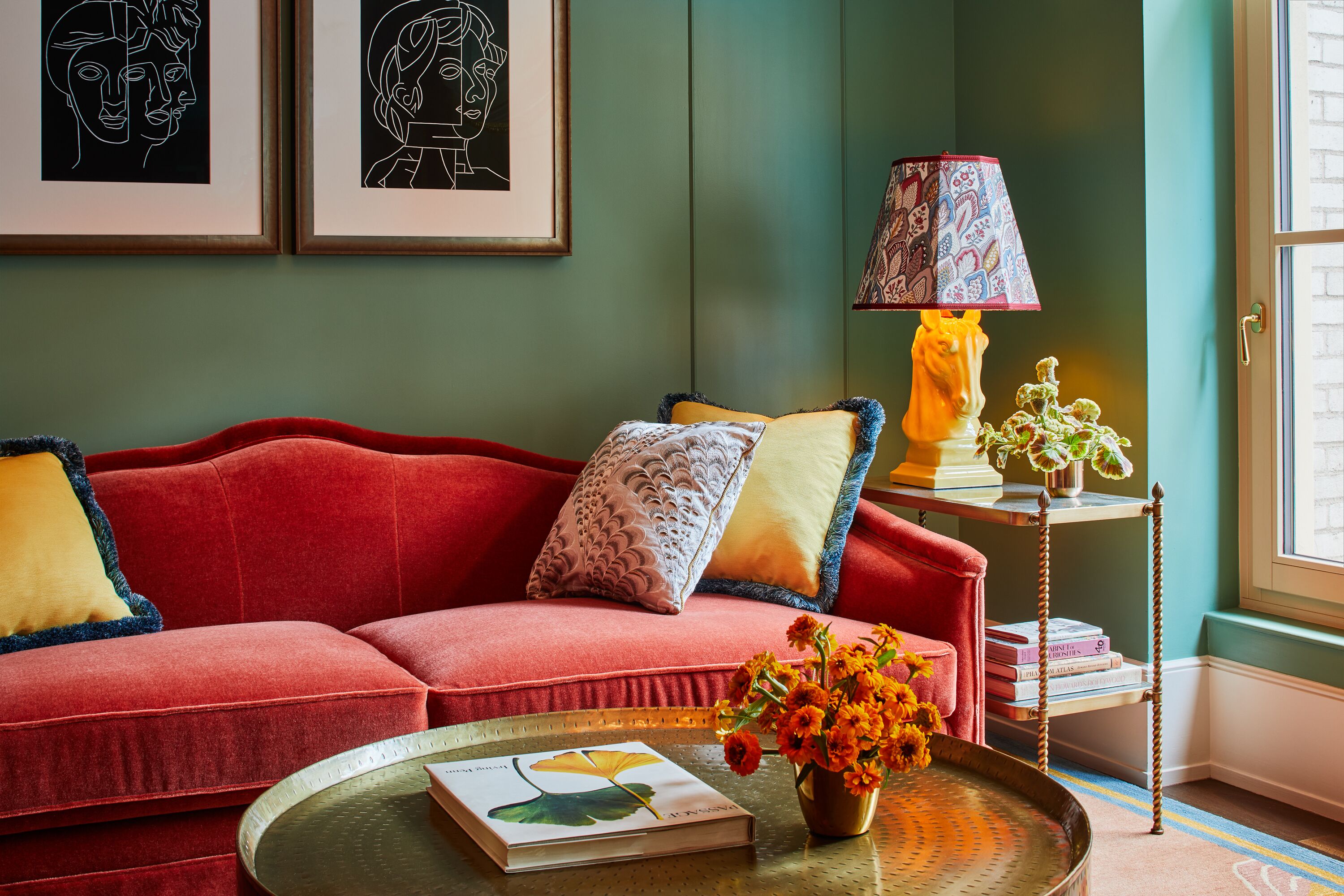 A cozy living room with a red sofa, a patterned lamp, and a vase with flowers.