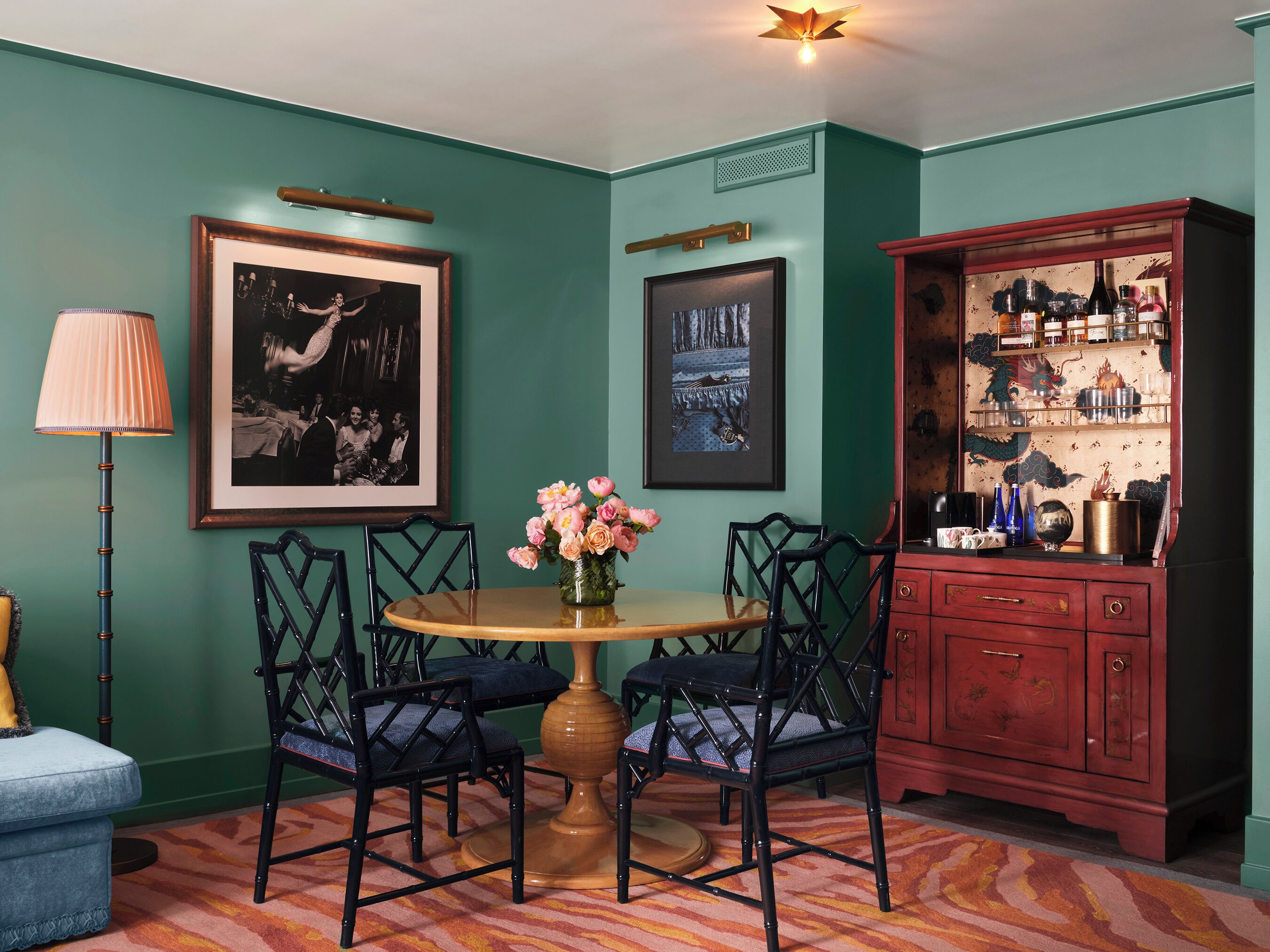 Um quarto com paredes verde-água, uma mesa redonda de madeira com cadeiras, um armário com portas de vidro e quadros nas paredes.
