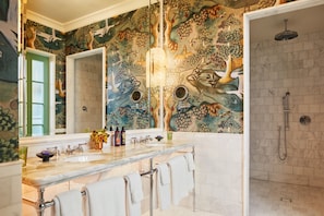Une salle de bain avec un grand miroir, un double vasque, une douche et une fresque murale.