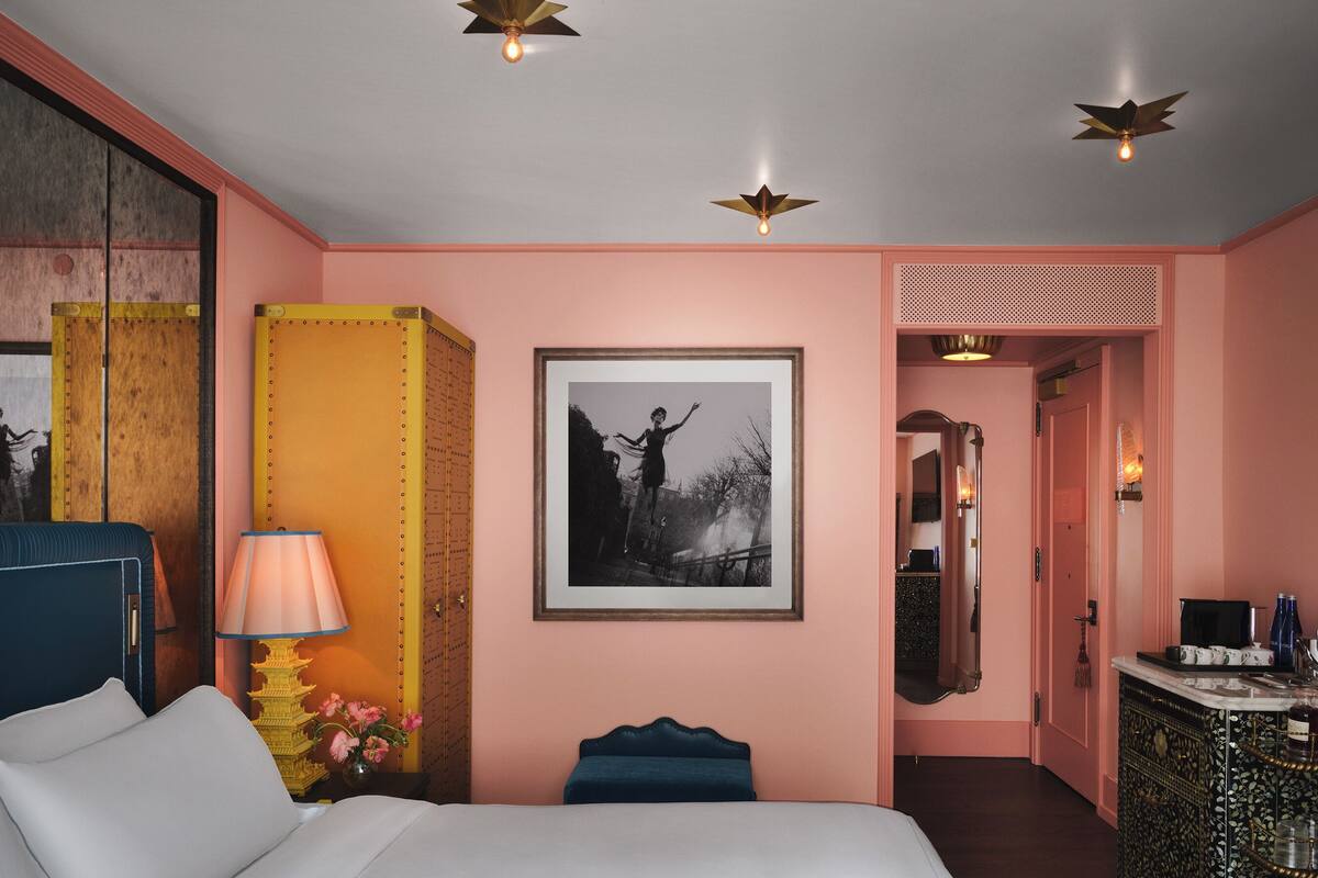 A hotel room with a bed, a desk, a chair, a lamp, a framed picture, and a decorative wall panel.