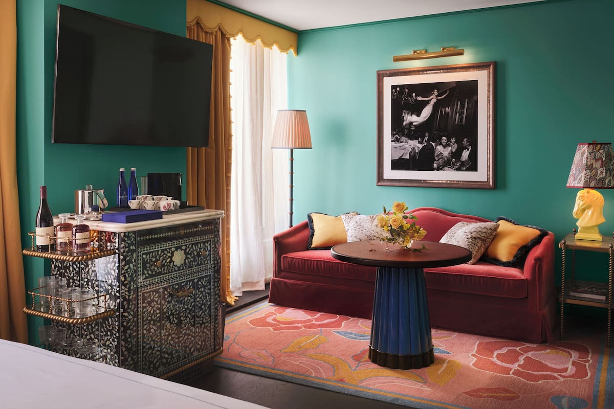 A room with a red sofa, a small round table with a vase, a television, a patterned cabinet, and a framed picture on the wall.
