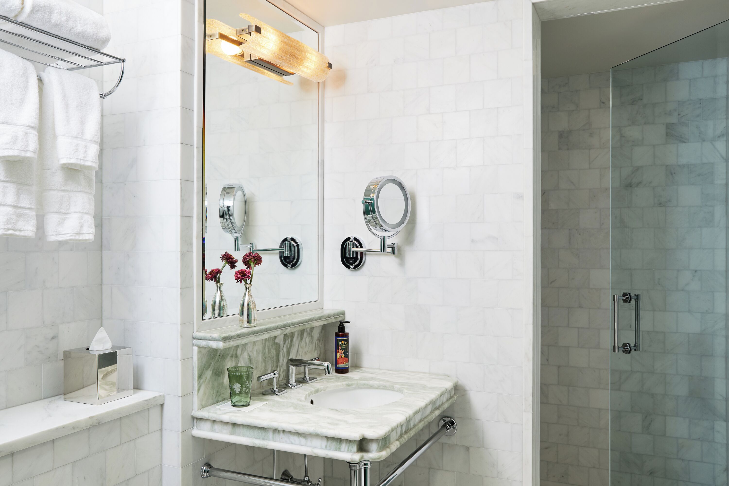 A bathroom with a marble sink, a mirror, a towel rack, and a glass shower enclosure.